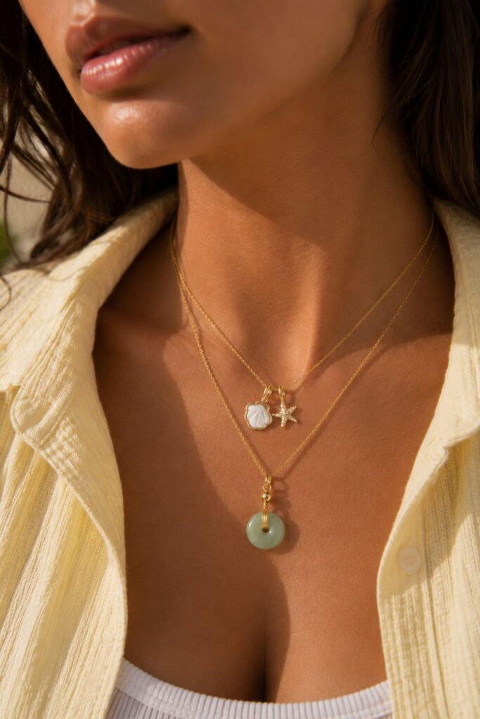 Woman wearing layered gold necklaces featuring a green jade gratitude necklace and a gold shell and starfish beach lover necklace styled for a chic coastal-inspired look.